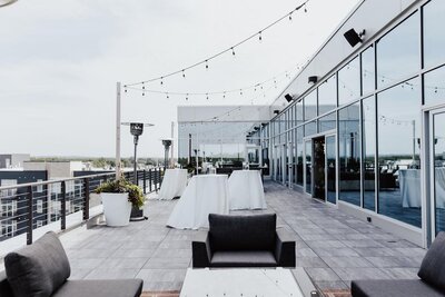 A rooftop balcony set up with cocktail tables, string lights, and lounge furniture.