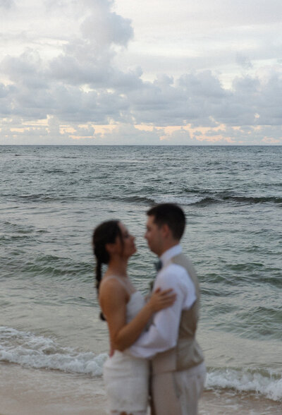 Bride and groom embracing on the beach at sunset during a destination wedding.