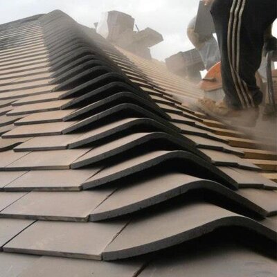 Roofer cutting roof tiles in place on a pitched roof.