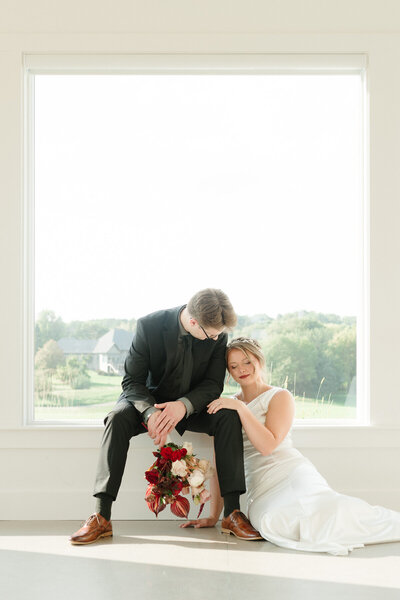 bride and groom sitting in front of large window