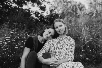 Adult sisters sitting at the ground looking straight to the camera and  leaning to each other in Helsinki in Finland