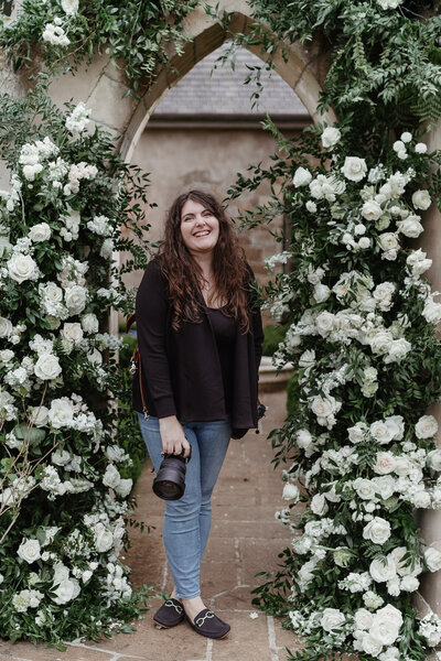 Vancouver WA Wedding Photographers Lindsey Wickert standing in a stone archway surrounded by flowers with her camera