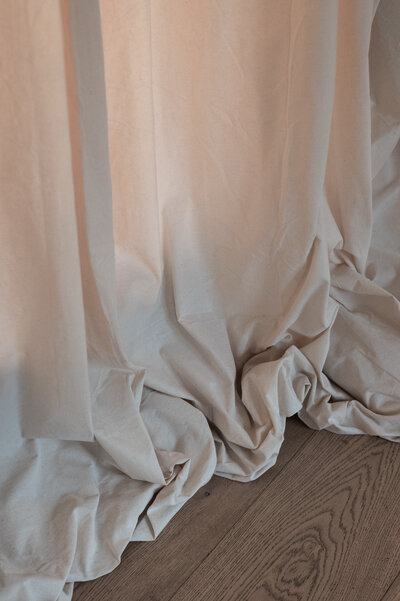 Neutral brand detail image of a curtain draped on a wooden floor.