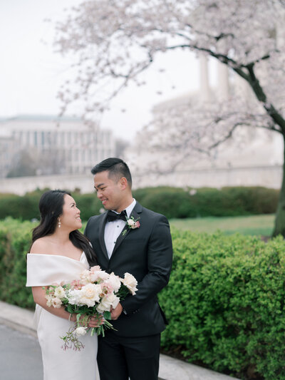 A bride and groom pose in from of Cherry Blossoms