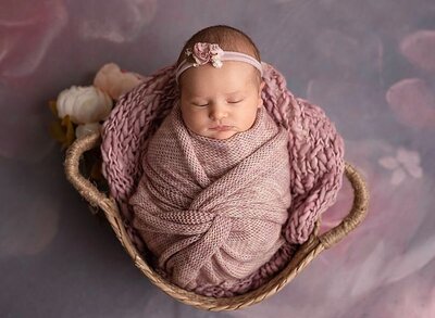 newborn baby girl, wrapped in pink, on knitted blanket in a prop