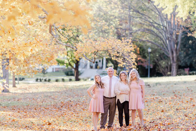 family of four standing closely together in a park on a sunny fall day