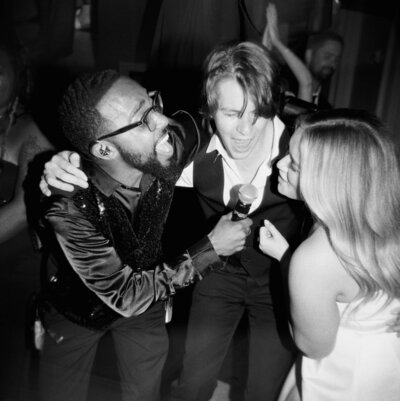 Candid black and white photo of the wedding couple singing into the microphone along with the singer of the band during their reception