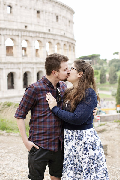 A newly engaged couple kissing in front of the Colosseum. Taken by Rome Surprise Photographer, Tricia Anne Photography.