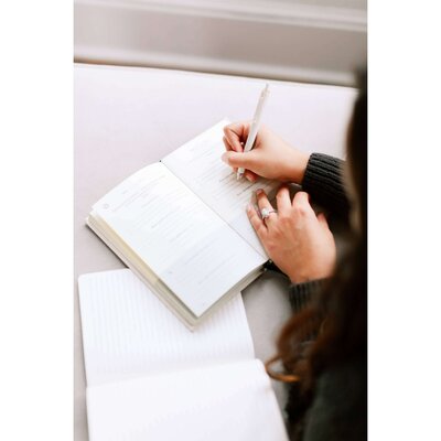 woman writing in a planner with dark hair and a wedding ring