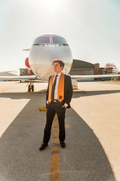 Purdue grad with graduation stole on posing in front of airplane