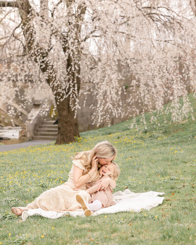 Mom kissing and embracing her child on a picnic blanket in a field at a park