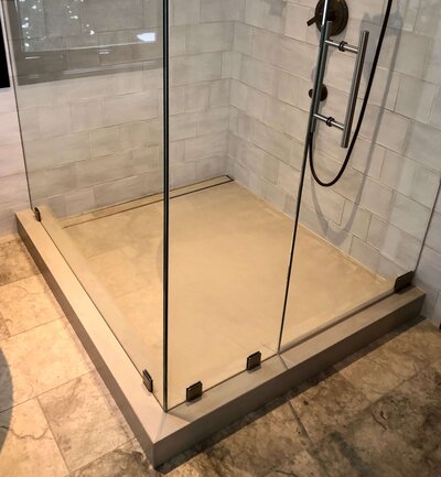 Concrete shower pan and curb in residential shower with seamless glass surround and tiles