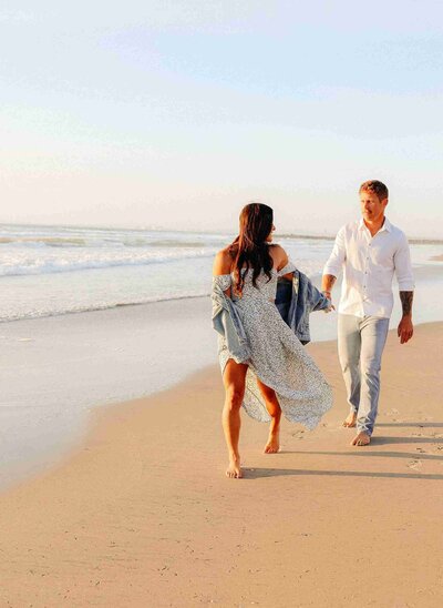 Hand in hand, a couple strolls along the beach, enjoying the sun and the sound of the waves.