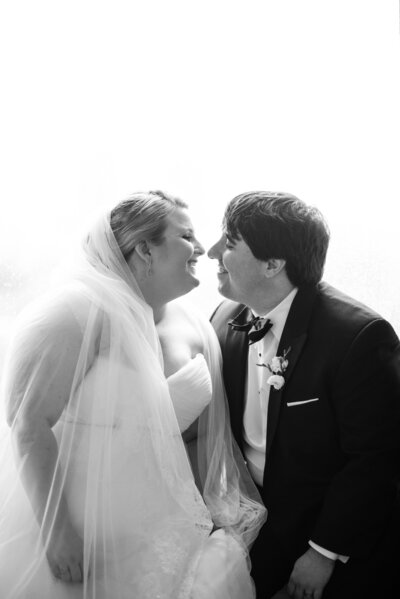 A bride and groom sitting next to each other leaning in for a kiss.