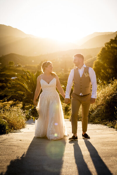 couple walking hand in hand with the sun setting over the mountains in the background