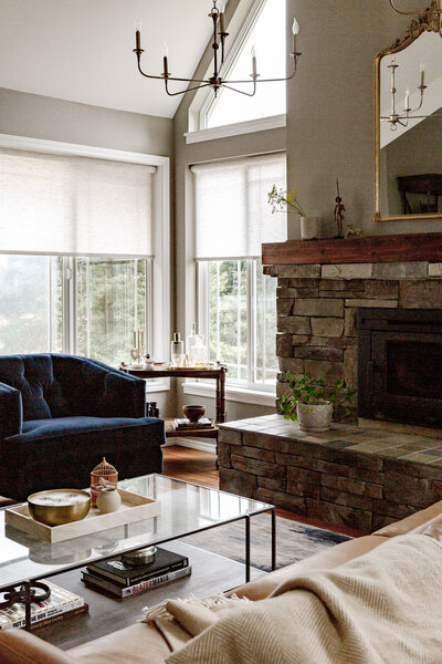 A living room featuring a stone fireplace, blue chair, and glass coffee table, representing a farmhouse interior design.