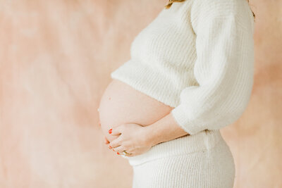 Maternity portrait of mother’s pregnant stomach against pink wall by Nashville Maternity Photographer