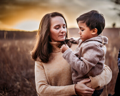 Family Photographers, Mom holds young son as he examines dry grass outside