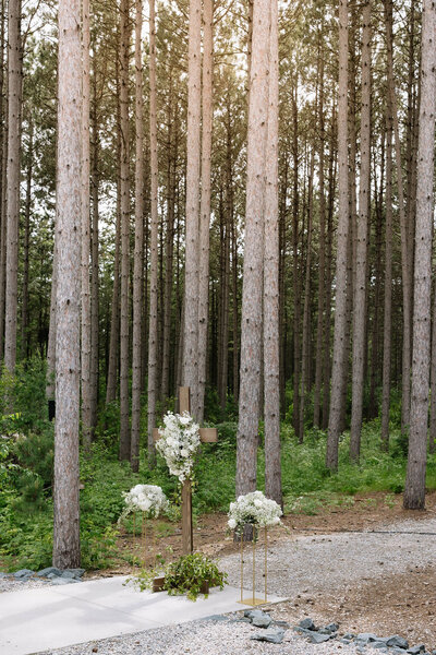 Beautiful white wedding flowers hung on a cross at the end of the walkway in a forest wedding in MN.