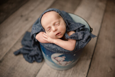 Newborn in teddy bear bucket with blue blankets around them