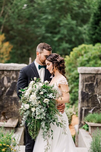 Bride and groom, embracing each other at Bella Luna farms, while bride has massive green bouquet with white flowers