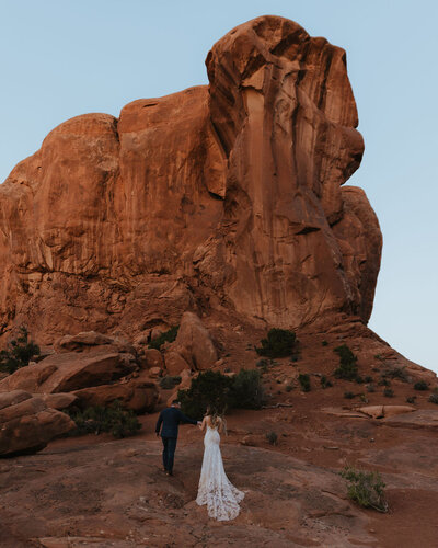 bride and groom walking in front of red rocks