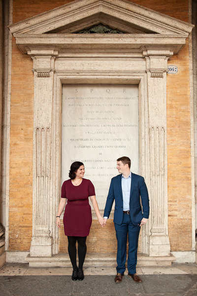 A couple holding hands in front of a Roman archway. Taken by Rome Honeymoon Photographer, Tricia Anne Photography