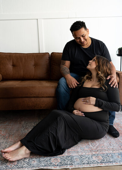 pregnant woman with fiance posing on a couch in a studio
