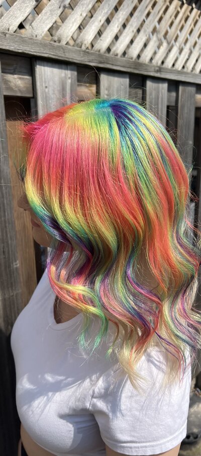 Image of client with hair that has been dyed a white blonde with a light, pastel, vivid, rainbow pattern.