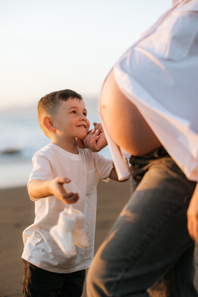 Mom wearing a red dress holding newborn baby up in a field during golden hour taken by a San Francisco Family photographer.