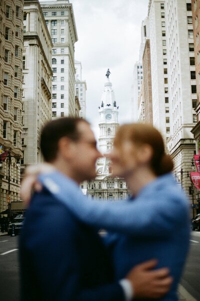 Bride and groom out of focus with the Philadelphia City Hall in the background