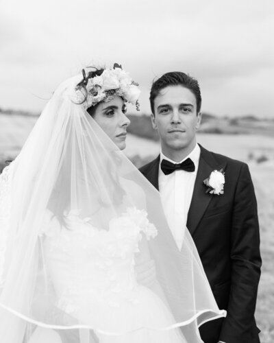 Wedding couple posing for their wedding photo in wedding attire. Groom is looking at the camera while the bride is looking away.
