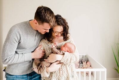 A couple affectionately looking at their baby in a nursery, captured during an in-home newborn photography session.