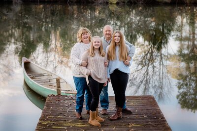 Family Portrait on the dock with canoe beside them and a reflction of the trees behind them in the water at Turnipseed Nursery in Fayetteville Georgia.
