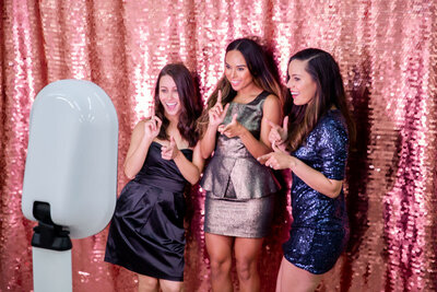 three women in front of a pink sequin backdrop posing in formalwear at a photo booth rental in West Chester
