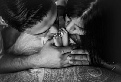 A loving couple kisses their newborn feet, their hands clasped together, symbolizing their deep connection.