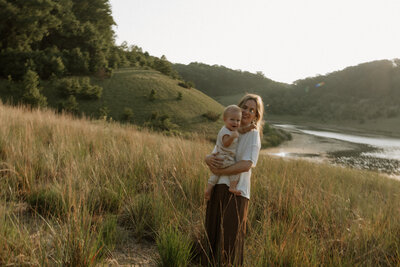 Kaity from Rainstorm Photo & Video holding her child in golden light at the Indiana Dunes, captured in a warm and candid documentary style.