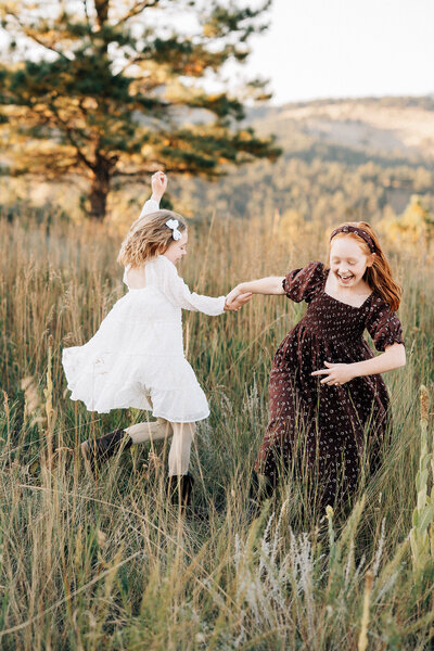 two sisters playing in tall grass swinging each other around