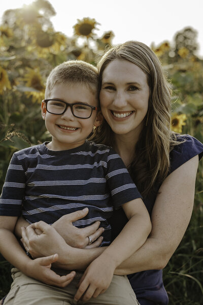 Verona B Photography captures a beautiful summer family photo of a mom holding her son and smiling at the camera at Medina Sunflower Farm in Medina, OH. The sunflowers were absolutely gorgeous on this lovely sunny day and it was so wonderful to capture this family in this beautiful setting near Akron.