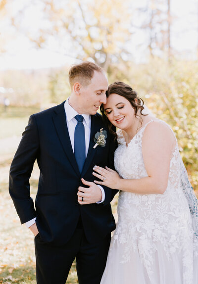 A bride and groom stand close together in the fall foliage in Calgary, Alberta