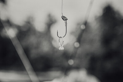 Close-up of fishing hook holding engagement ring during outdoor lifestyle session in New Braunfels, Texas.
