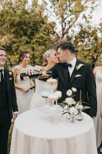Champagne tower and wedding couple kissing in the garden at Rouge Restaurant in Calgary