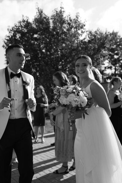 Soft black and white photo of newlyweds sharing joyful moment outdoors after Greek Orthodox wedding ceremony.