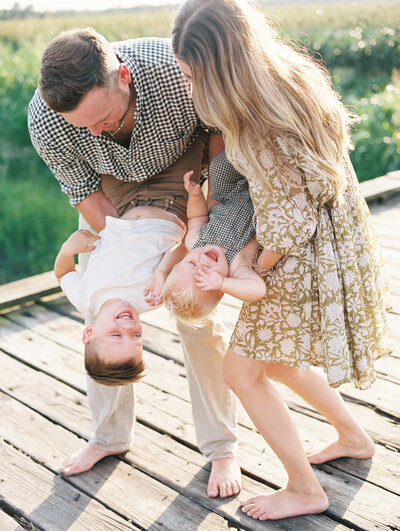 Mom and dad holding their 2 kids upside down