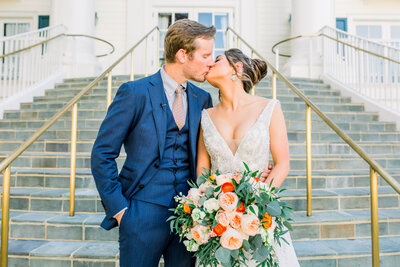 Just married couple kissing  during couple's portraits while holding a beautiful bouquet of flowers.