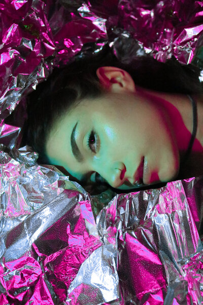 Close-up artistic portrait of photographer surrounded by colored lights and reflective foil.