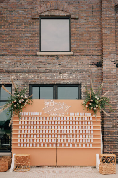 A wedding seating chart that is rust colored and says "Let's get this party started" at The River Center, a des moines iowa wedding venue. Photo by Anna Brace, an iowa wedding photographer.