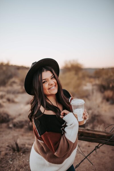 woman wearing black brim hat with coffee smiling