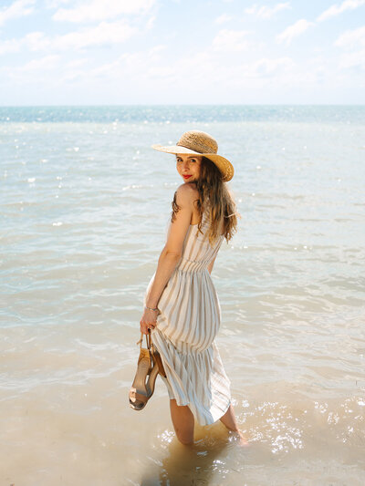 Kilee in a striped dress and straw hat standing in the ocean