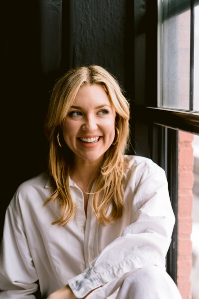 woman in a white linen shirt looking towards the window while smiling